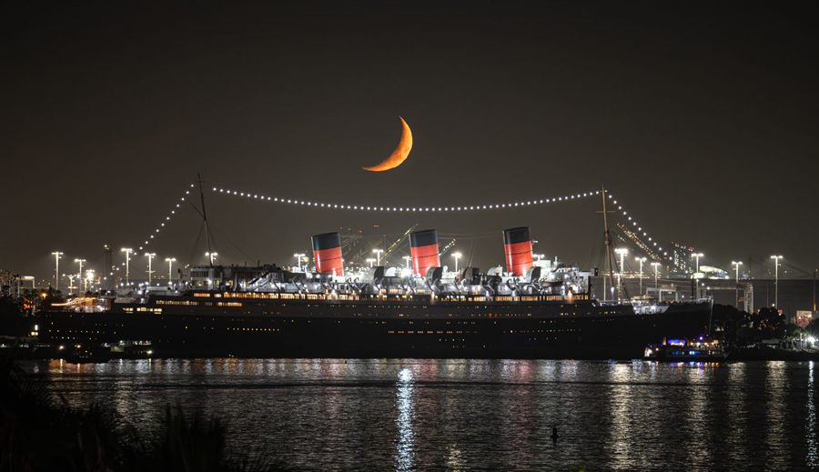 The historic liner Queen Mary illuminated at night under a crescent moon
