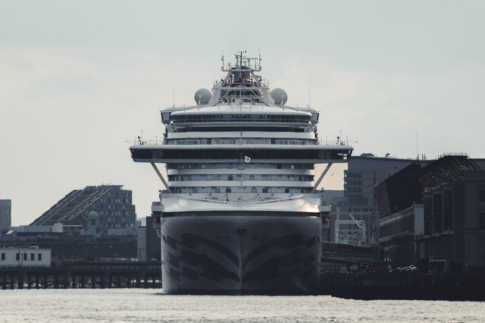 Massive cruise ship docked bow-on in a city harbor surrounded by tall buildings