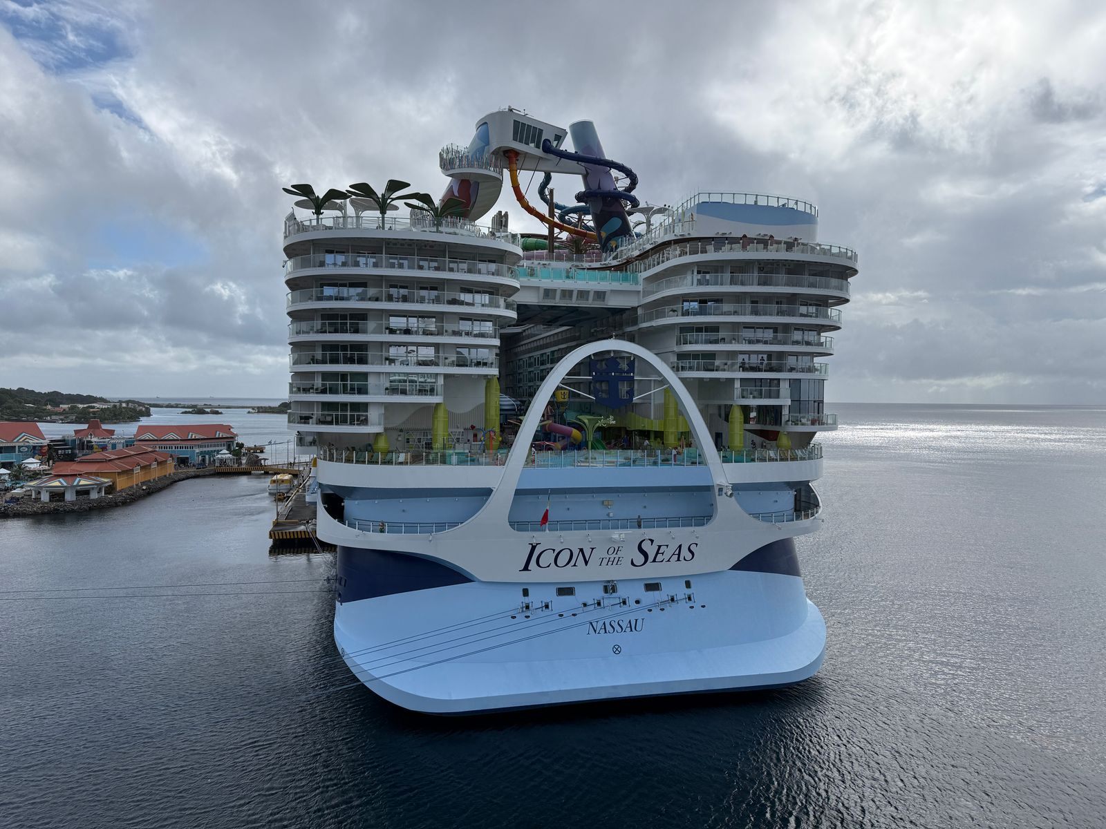 Royal Caribbean’s Icon of the Seas, the world’s largest cruise ship, docked in a harbor with its glass dome and water slides visible