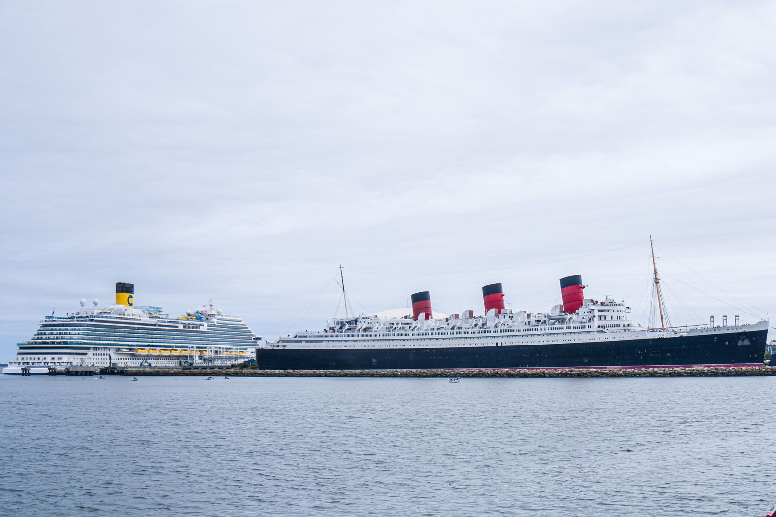 The classic liner Queen Mary beside a modern cruise ship in Long Beach, the old and new eras behind the biggest cruise ship compared to Titanic