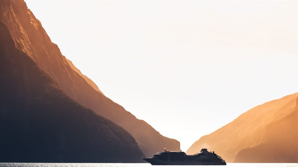 Cruise ship silhouetted between steep cliffs in a New Zealand fjord at sunset